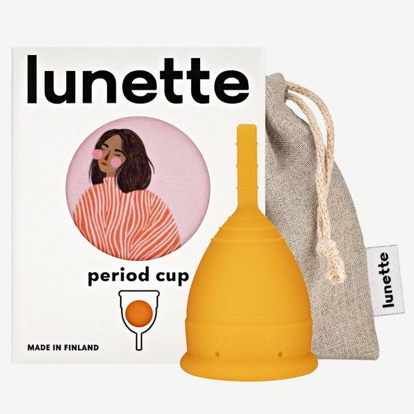 An orange Lunette period cup displayed alongside its packaging box with a floral design and a linen storage pouch. The box includes the text 'period cup', 'made in Finland', and the brand name 'Lunette'.